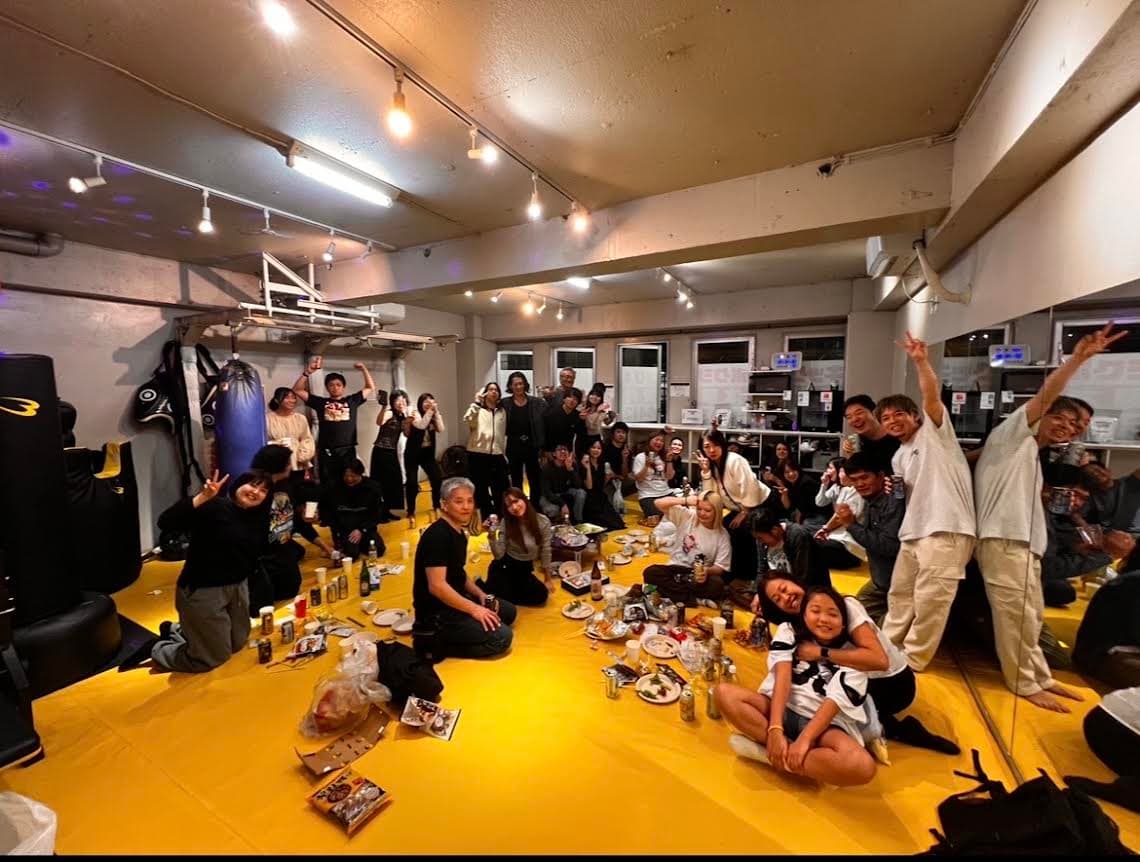 黄色マットのジム内で会員同士が飲み会を楽しむ様子