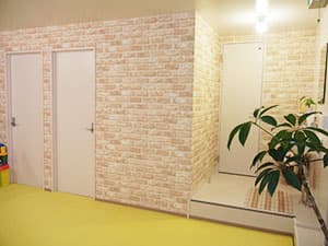 レンガ調の壁と白い扉、黄色い床の廊下（更衣室・シャワー室エリア）